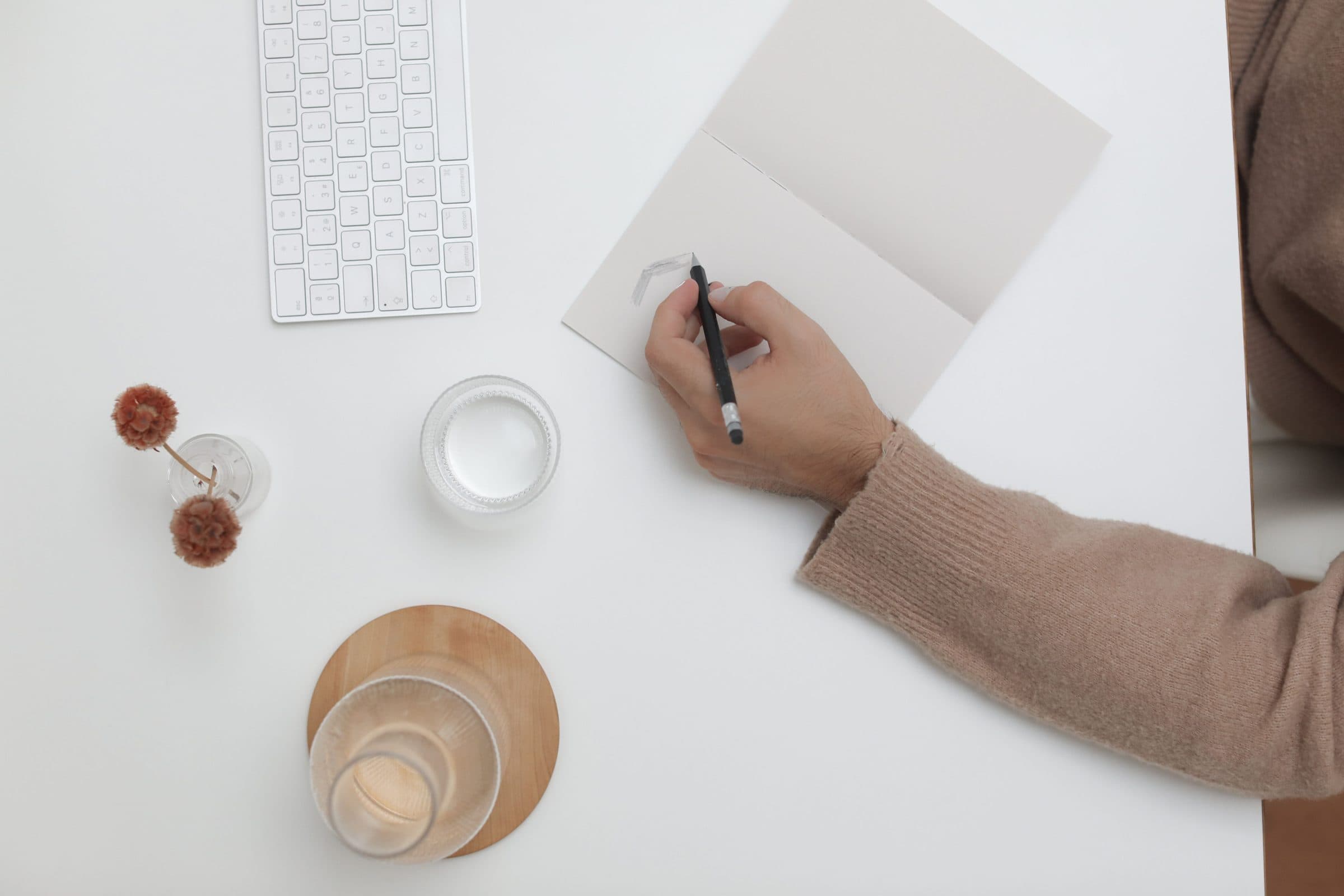 An overhead view of someone writing a card at a bright desk