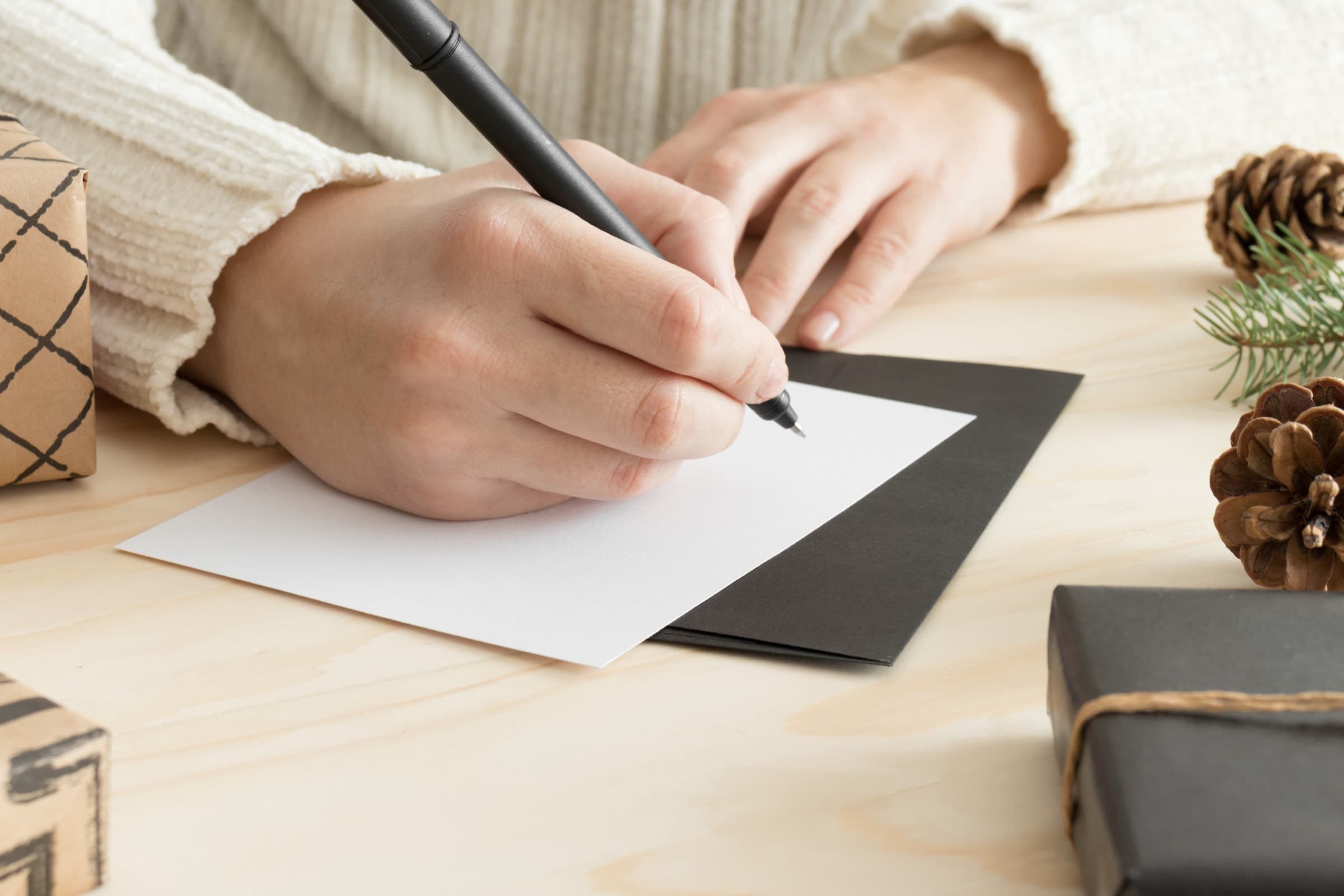 A hand writing a note on a card with a black pen